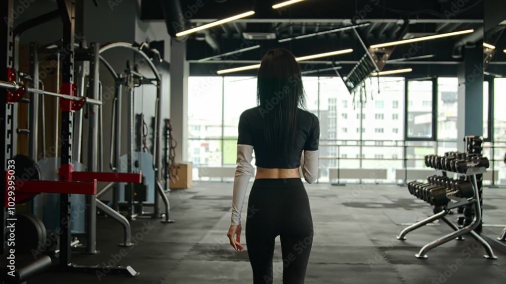 Back view unknown fit sportswoman girl athletic slim woman personal fitness trainer workout instructor walking in gym with sports equipment client of sport club going drink water drinking from bottle Back view unknown fit sportswoman girl athletic slim woman personal fitness trainer workout instructor walking in gym with sports equipment client of sport club going drink water drinking from bottle