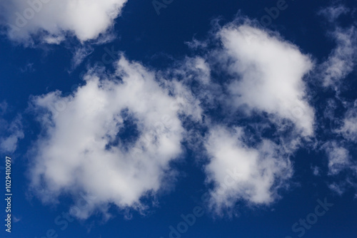 Soft white cloud in a blue sky. Puffy cloud with sunlight. Dark blue sky background. Single cloud shape. Heavenly atmosphere. Bright sky pattern. Round shape with a hole inside.