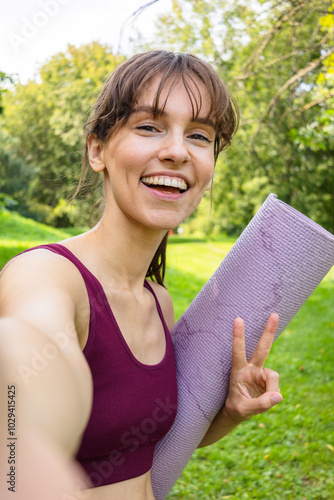 Brunette fit yoga girl with a beautiful smile taking selfie in the green park in summer