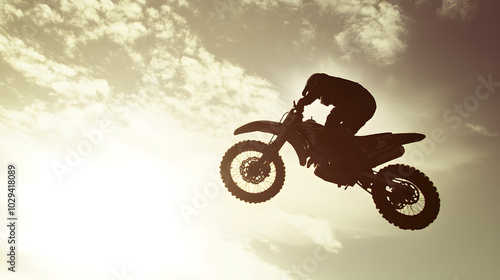 A motorcycle stunt rider mid-air during a backflip silhouetted against a bright afternoon sky. photo