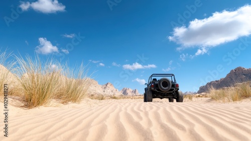 An SUV traverses rugged desert terrain under a clear blue sky, emphasizing adventure and resilience, with surrounding grass patches and rocky formations visible. photo