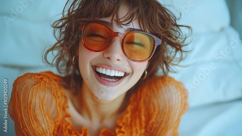 A cheerful woman laughing while wearing stylish sunglasses, showcasing her vibrant hairstyle and joyful expression indoors during daylight