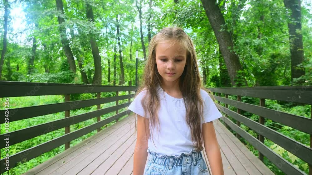 portrait little child in green forest slow motion. Happy kid girl walk on wooden bridge in nature park on summer vacation portrait little child in green forest slow motion. Happy kid girl walk on wooden bridge in nature park on summer vacation