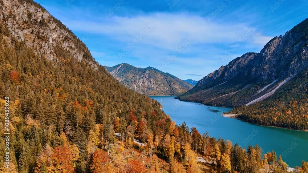 Trees covering the picturesque mountains are starting to change colors in autumn. Drone footage over the spectacular Lake Plansee locating in the Alps. Reutte District, Tyrol, Austria. Trees covering the picturesque mountains are starting to change colors in autumn. Drone footage over the spectacular Lake Plansee locating in the Alps. Reutte District, Tyrol, Austria.