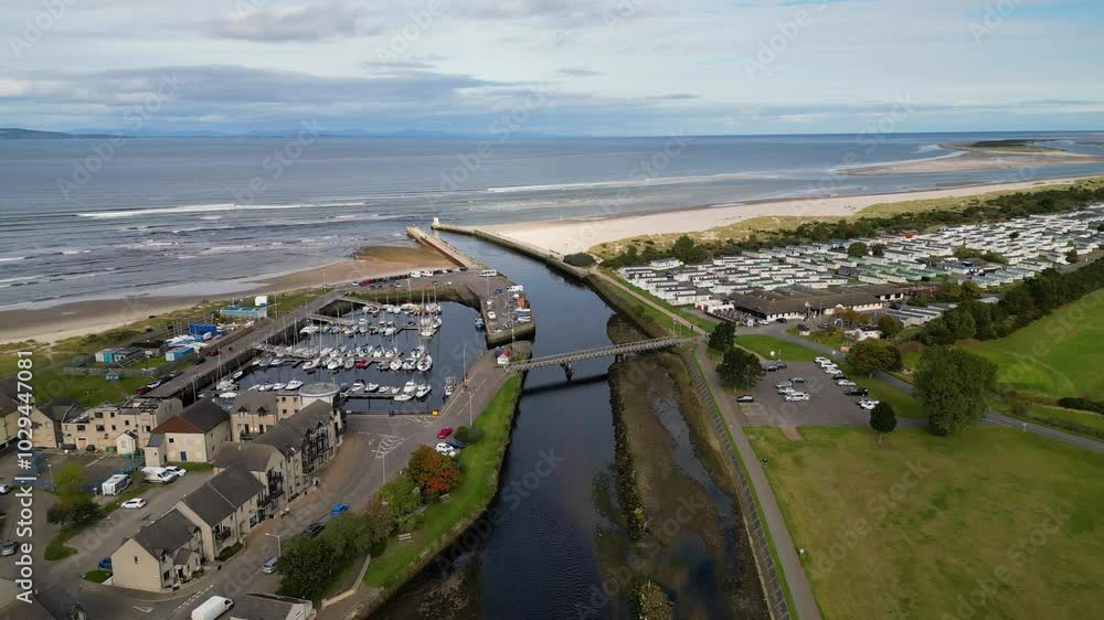 Aerial view down a river flowing past a harbour and bridge, then into the ocean via a sea wall / breakwater. Nairn, Scotland. Aerial view down a river flowing past a harbour and bridge, then into the ocean via a sea wall / breakwater. Nairn, Scotland.