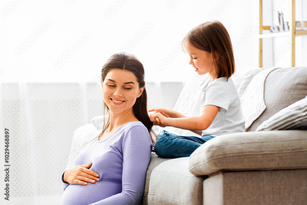 Cute little girl brushing her smiling pregnant mom hair, home interior, free space Cute little girl brushing her smiling pregnant mom hair, home interior, free space
