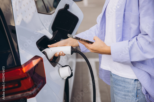 Woman Charging Electric Car While Using Smartphone at Modern Charging Station photo