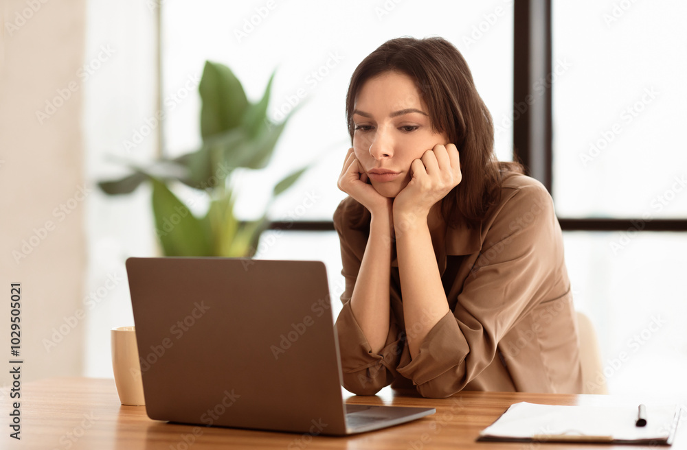 Missing Deadlines. Disappointed cute secretary using laptop sitting at desk in modern office, looking away, copyspace Missing Deadlines. Disappointed cute secretary using laptop sitting at desk in modern office, looking away, copyspace