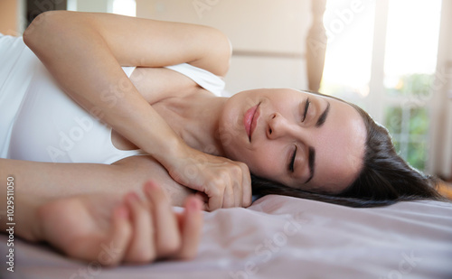 A peaceful woman is resting on her side in bed, eyes closed, with a soft expression. Sunlight gently fills the room, creating a serene and cozy atmosphere, ideal for moments of relaxation or napping