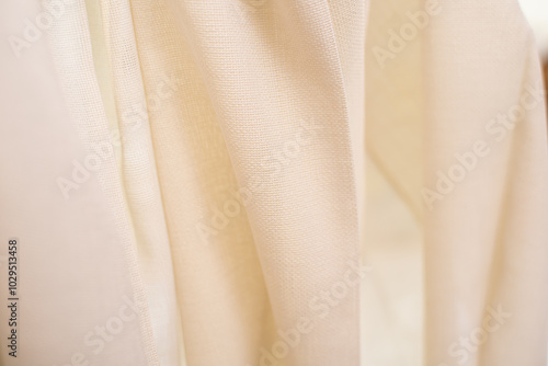 Close up of light beige fabric with a semi transparent, woven texture. The fabric is softly draped. photo