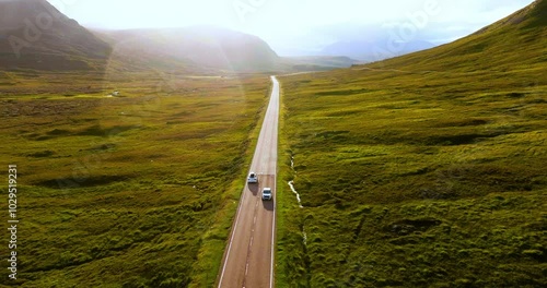 Aerial shot of white electric car traveling through breathtaking sunny landscape in the Highlands Scotland