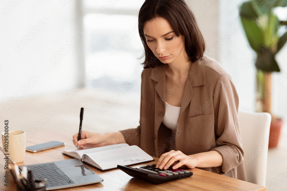 Budget Planning. Focused young woman using calculator, counting income and expenses and writing, free space Budget Planning. Focused young woman using calculator, counting income and expenses and writing, free space