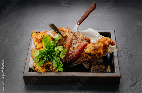 Roasted pork knuckle with potatoes and fresh herbs on wooden tray, stock food photography photo