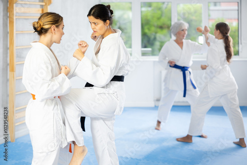 Experienced Asian female karateka in kimono and black belt honing kicking techniques during kumite at training session photo