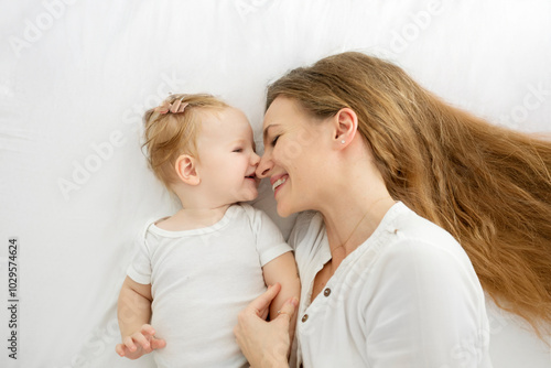 Loving mother lying with her cute little baby girl on the bed, enjoying motherhood time and maternity leave, top view