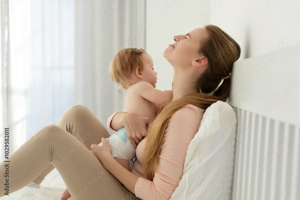 Tired crying young mother suffering from experiencing postnatal depression, sitting on bed and holding baby on hands Tired crying young mother suffering from experiencing postnatal depression, sitting on bed and holding baby on hands