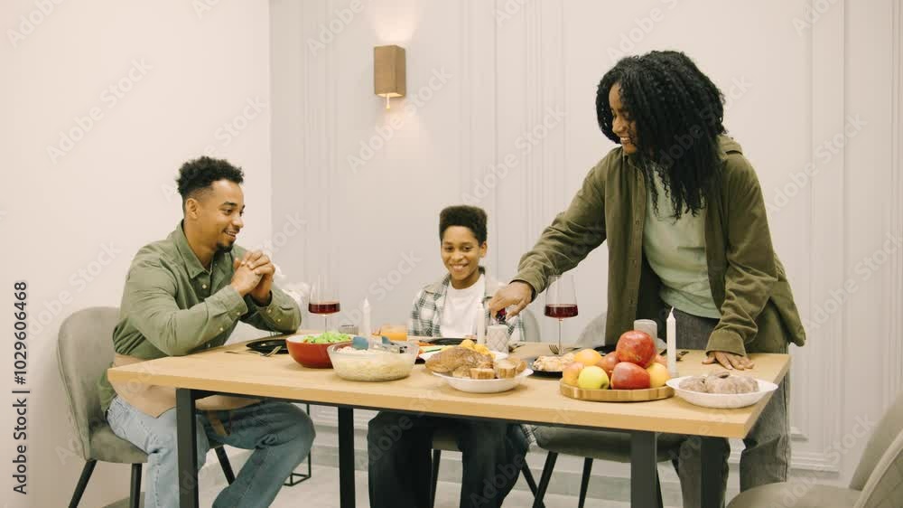 An African American Mother Lights Candles on a Festive Family Table to Create a Cozy and Romantic Atmosphere for the Celebration An African American Mother Lights Candles on a Festive Family Table to Create a Cozy and Romantic Atmosphere for the Celebration