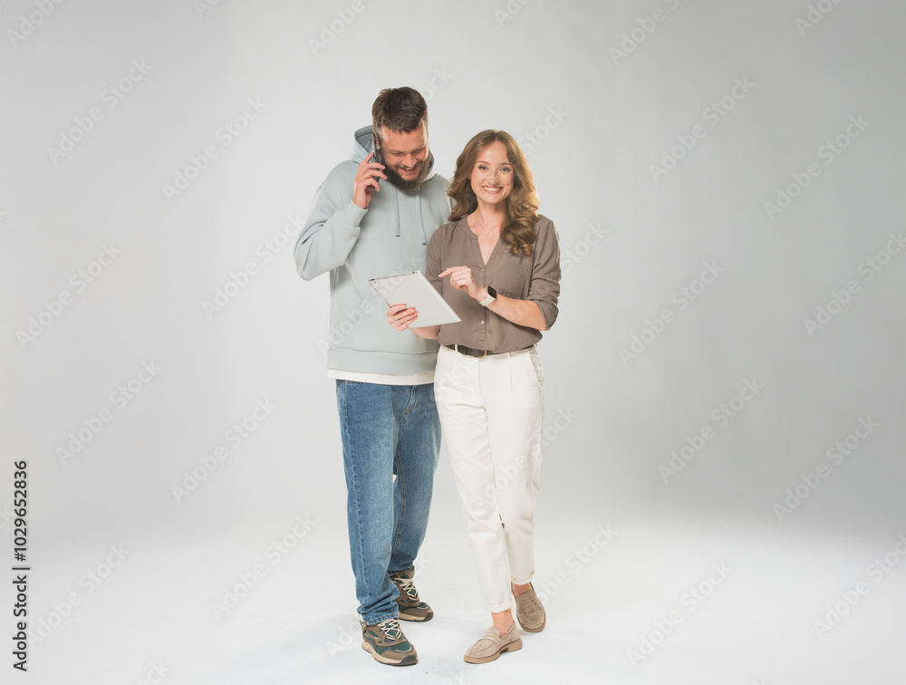 A man and a woman in full growth on a white background use a tablet and a smartphone approve recommend something. A man and a woman in full growth on a white background use a tablet and a smartphone approve recommend something.