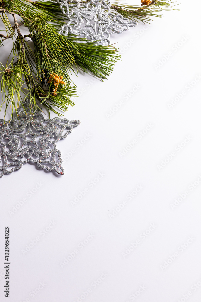 Fototapeta premium Pine branches and silver stars adorn the top corner of a white background with copy space