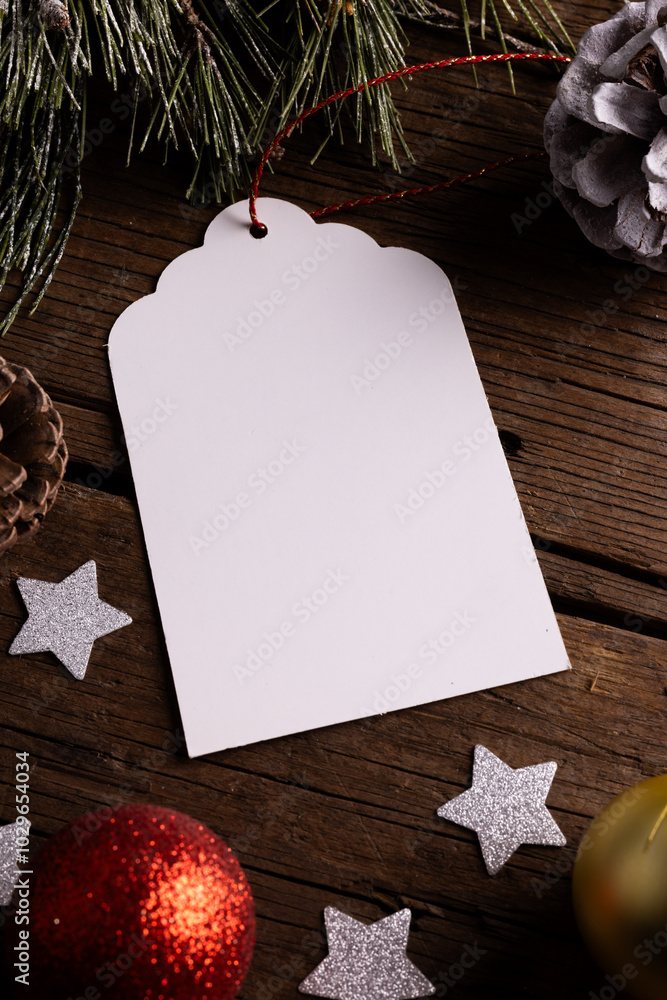 Fototapeta premium A blank Christmas tag lies on a wooden surface with copy space, surrounded by festive decorations