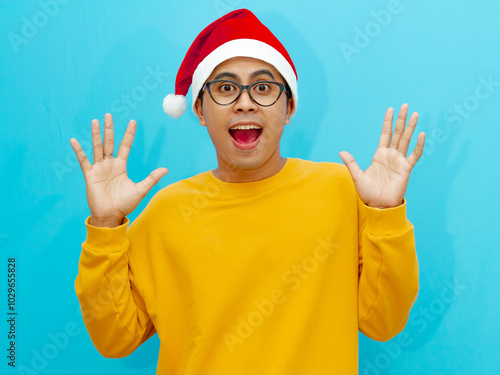 Excited young Asian man in a Christmas hat showing a surprised expression while looking at the camera. photo