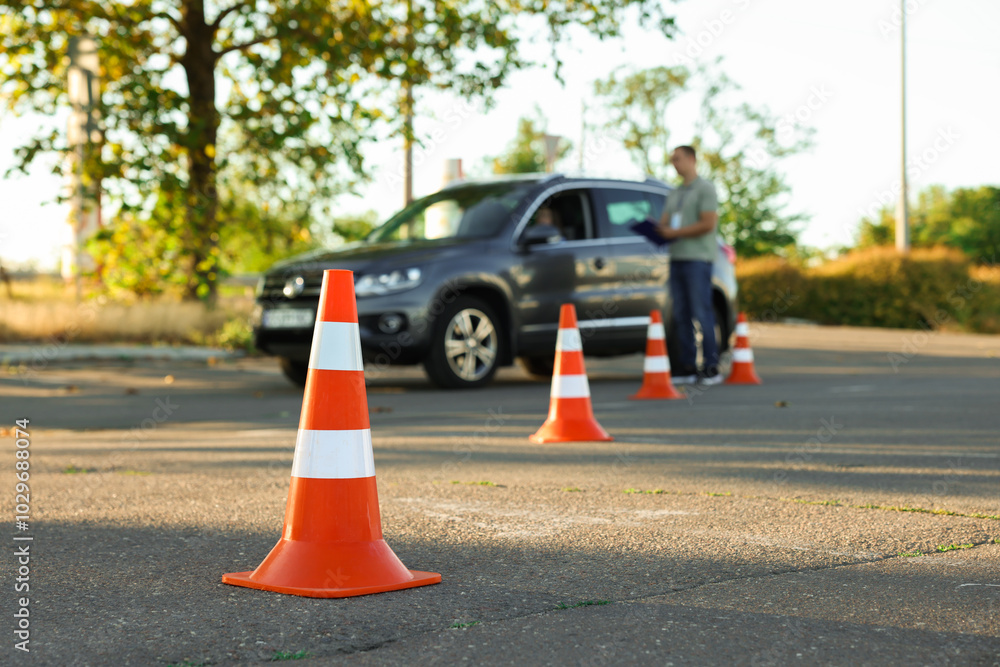 Examiner instructing student before exam at driving school test track, focus on traffic cone Examiner instructing student before exam at driving school test track, focus on traffic cone