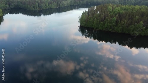 Glassy deep blue lake surface reflects clouds in blue sky, green forest photo