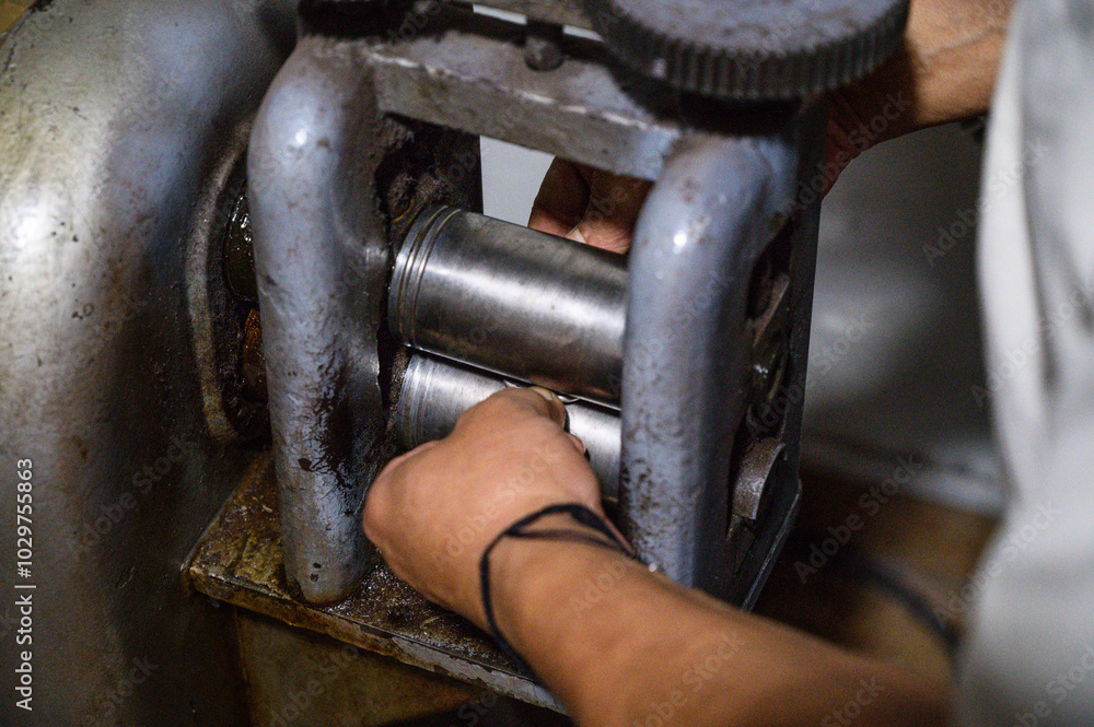 Goldsmith is working on a piece of metal using a traditional rolling mill in a workshop