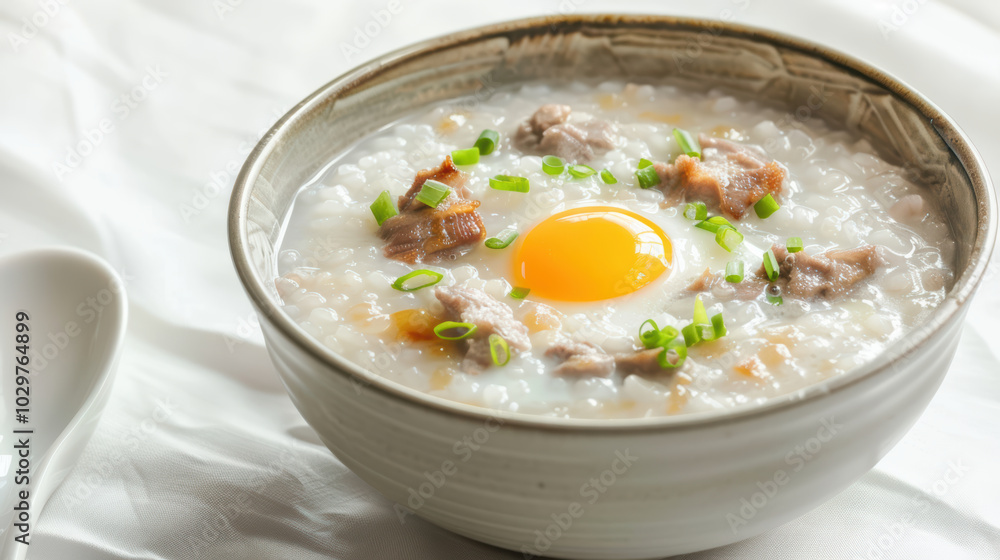 Creamy rice porridge topped with tender meat, sunny egg yolk, and fresh green onions creates comforting and delicious meal. Perfect for breakfast or any time of day Creamy rice porridge topped with tender meat, sunny egg yolk, and fresh green onions creates comforting and delicious meal. Perfect for breakfast or any time of day