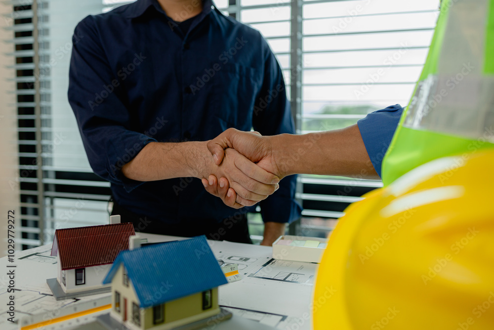 engineer and architect are shaking hands to celebrate because they just finished big construction project, two engineers do handshake after the meeting, blueprint is on the desk engineer and architect are shaking hands to celebrate because they just finished big construction project, two engineers do handshake after the meeting, blueprint is on the desk