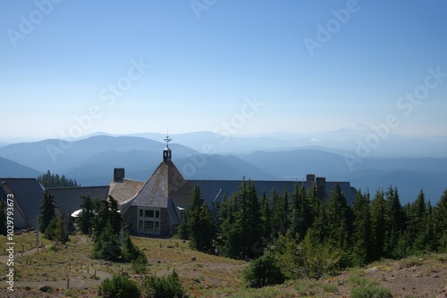Timberline Lodge nestled between some pine trees with a cascade range disappearing in to clouds and mist in the background.