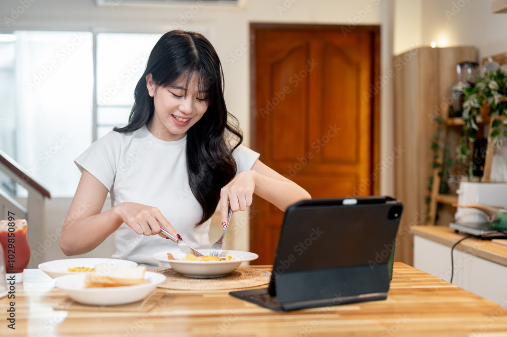 A beautiful Asian woman is enjoying her breakfast while watching something on her digital tablet. A beautiful Asian woman is enjoying her breakfast while watching something on her digital tablet.