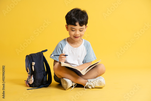 Full body image of a boy holding books, backpack and posing on a yellow background photo