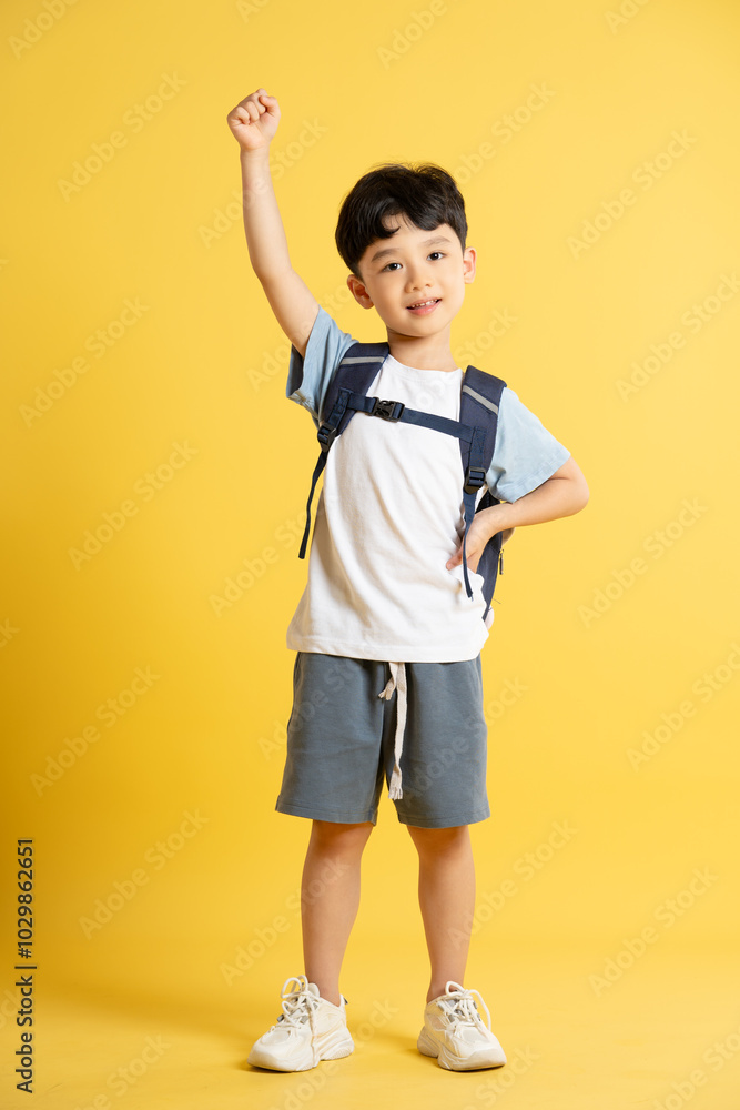 Full body image of an Asian boy wearing a school backpack and posing on a yellow background Full body image of an Asian boy wearing a school backpack and posing on a yellow background
