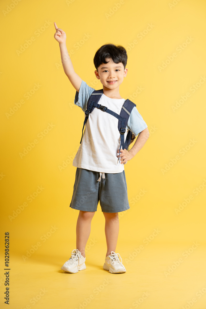 Full body image of an Asian boy wearing a school backpack and posing on a yellow background Full body image of an Asian boy wearing a school backpack and posing on a yellow background
