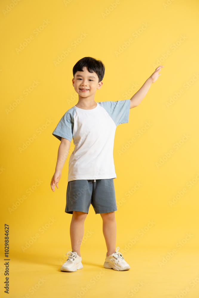Full body image of asian kid boy wearing summer clothes posing on yellow background Full body image of asian kid boy wearing summer clothes posing on yellow background