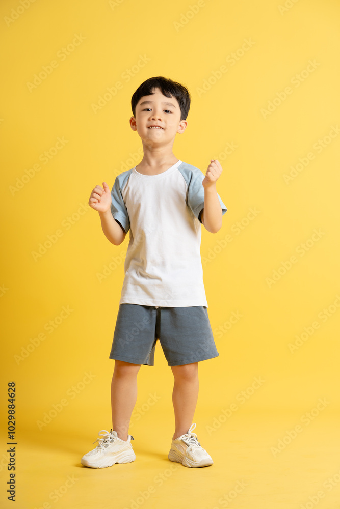 Full body image of asian kid boy wearing summer clothes posing on yellow background Full body image of asian kid boy wearing summer clothes posing on yellow background