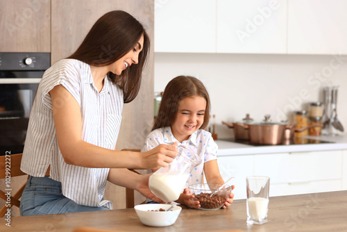 Happy mother with her little daughter having breakfast in kitchen