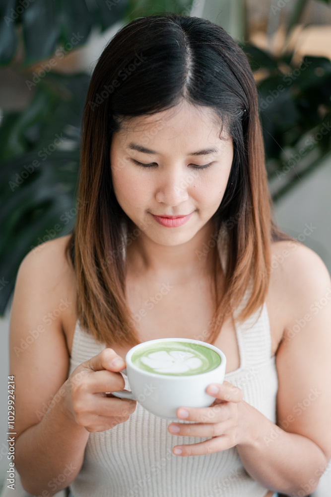 A young woman holding a cup of matcha latte, enjoying a peaceful moment in a cozy cafe with lush green plants in the background. A young woman holding a cup of matcha latte, enjoying a peaceful moment in a cozy cafe with lush green plants in the background.