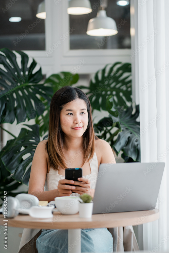 A young woman using a laptop and smartphone in a modern home office setting with green plants in the background. A young woman using a laptop and smartphone in a modern home office setting with green plants in the background.