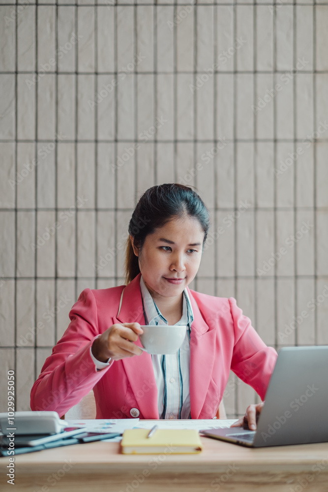 Professional woman in pink blazer working on a laptop and holding a coffee cup, set in a modern office environment. Professional woman in pink blazer working on a laptop and holding a coffee cup, set in a modern office environment.
