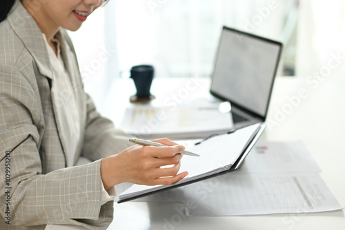 A woman is writing with a pen on a piece of paper. She is wearing a gray jacket and is sitting at a desk.