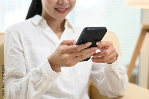 A woman is sitting on a couch and using her cell phone. She is smiling and she is happy.