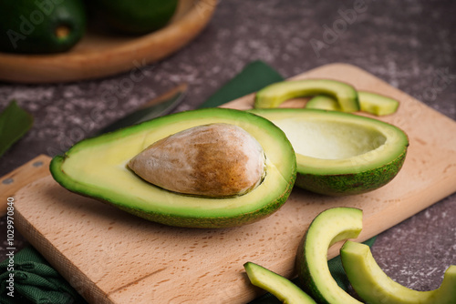 Wooden board with cut fresh avocados on dark background photo