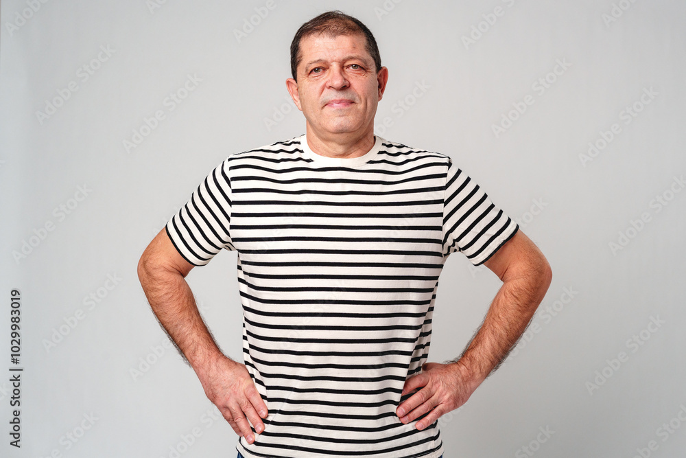 A man stands confidently in a striped shirt, casual jeans with a neutral background A man stands confidently in a striped shirt, casual jeans with a neutral background