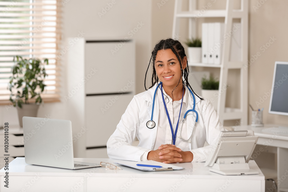Young African-American female doctor sitting at table in clinic Young African-American female doctor sitting at table in clinic