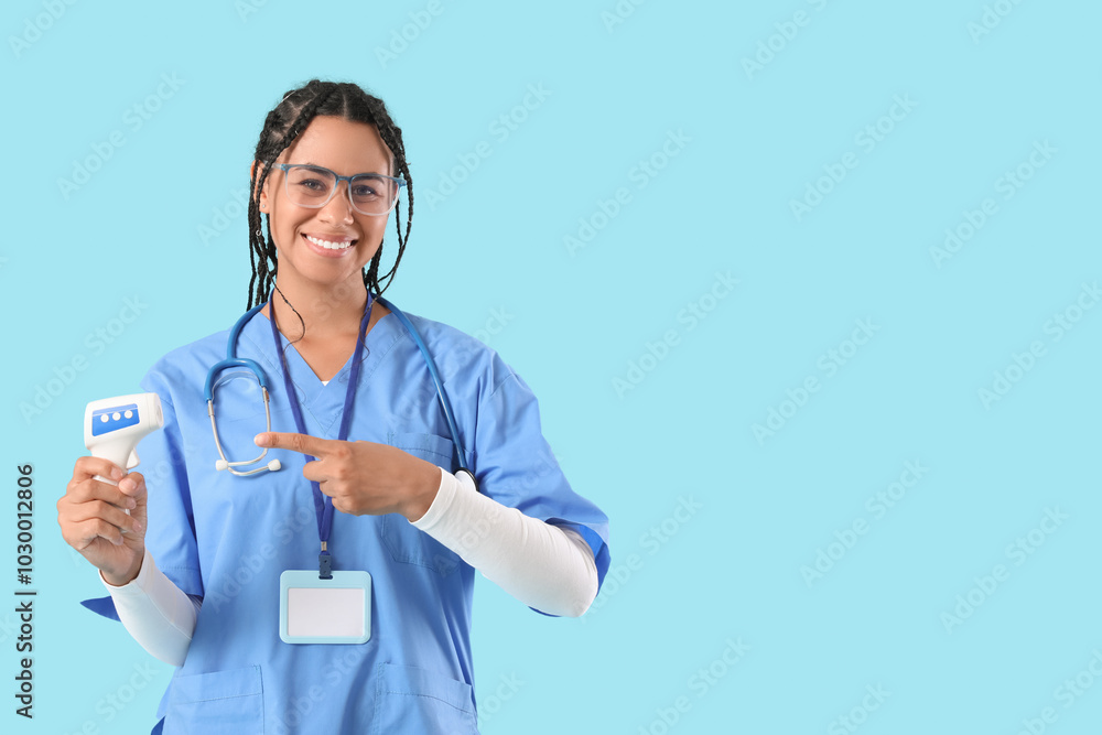 Young African-American female doctor with stethoscope pointing at thermometer on blue background Young African-American female doctor with stethoscope pointing at thermometer on blue background