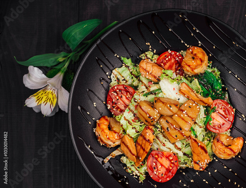 Delicious warm salad with grilled chicken, king prawns and sesame seeds being served on black plate photo