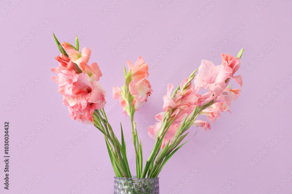 Glass vase with bouquet of beautiful gladiolus flowers on lilac background Glass vase with bouquet of beautiful gladiolus flowers on lilac background