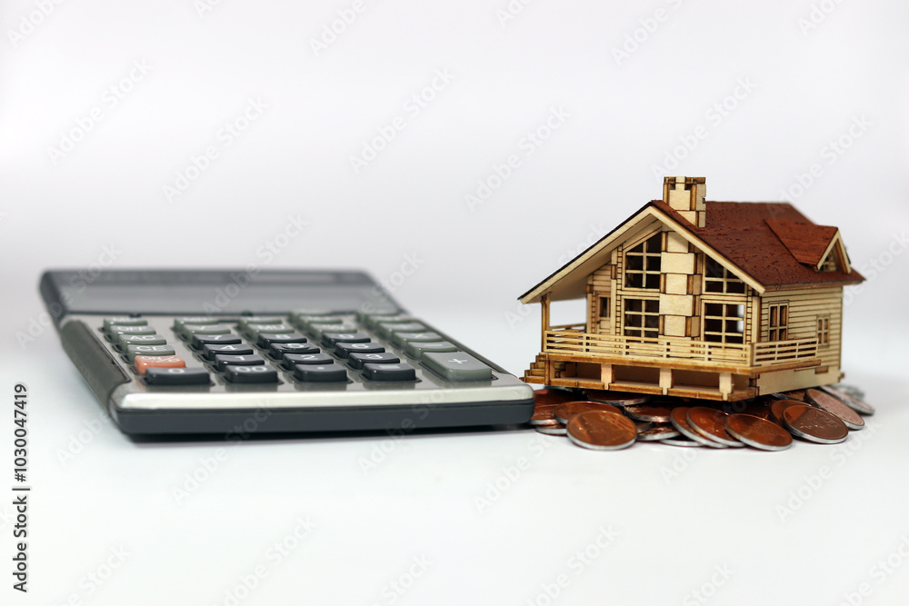 A house is placed on a pile of calculators and coins against a white background. Instability in the real estate market.
